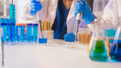 Obraz na płótnie Two Asian female scientists wearing laboratory gloves sit at a table, carefully examining a test tube filled with blue liquid, using a microscope for detailed analysis in a research laboratory w salonie