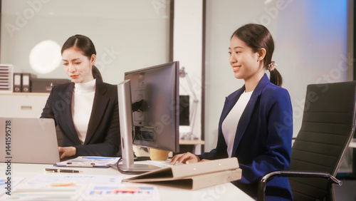 Obraz na płótnie Two young Asian business woman sit at a table in the office, discussing marketing strategies, using a computer reviewing documents with charts and graphs, collaborating on new business plans at work w salonie