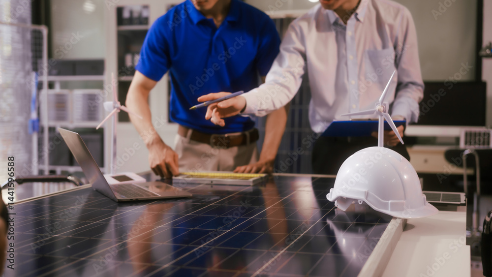 Two Asian businessmen wearing engineer hats table, discussing solar panels and wind turbines. They plan environmental projects, focusing on solar energy solutions and renewable energy installations