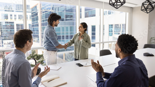 Boss praising proud Indian female employee, congratulating with corporate success, handshaking, express appreciation and recognition, colleagues clap hands, supporting mate during meeting in boardroom