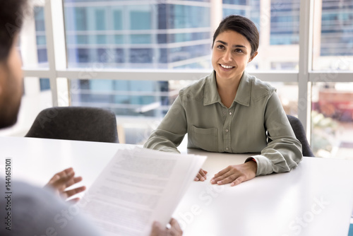 Young Indian woman applicant sit at table in modern office during job interview. Formal meeting between two businesspeople, discuss contract terms and conditions. Confidence, ambition, career growth