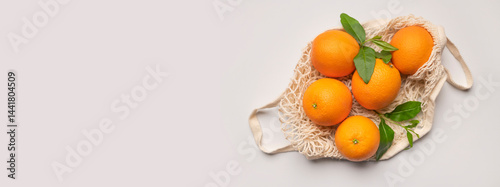 Ripe juicy oranges in cotton string bag on light gray background. Eco-friendly thread bag for shopping, buying food, fruits, vegetables. Zero waste, plastic free concept. Empty space for text