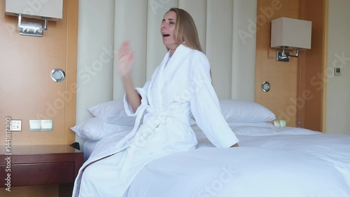 A woman wakes up in the morning in white pastels in hotels and wakes up satisfied and gets up. Good mood, smile and positive attitude for the day, vacation, vacation for mom in a bathrobe. High