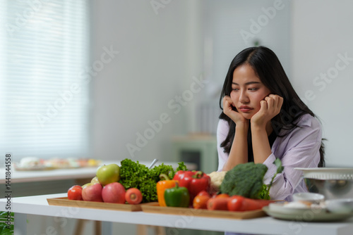Canvas-taulu Sad asian woman looking at a variety of fresh vegetables and fruits while sittin