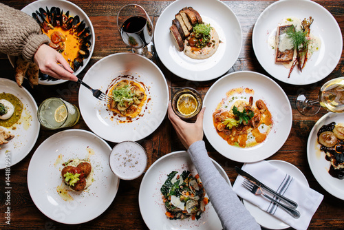 Two female hands reaching over tabletop food spread