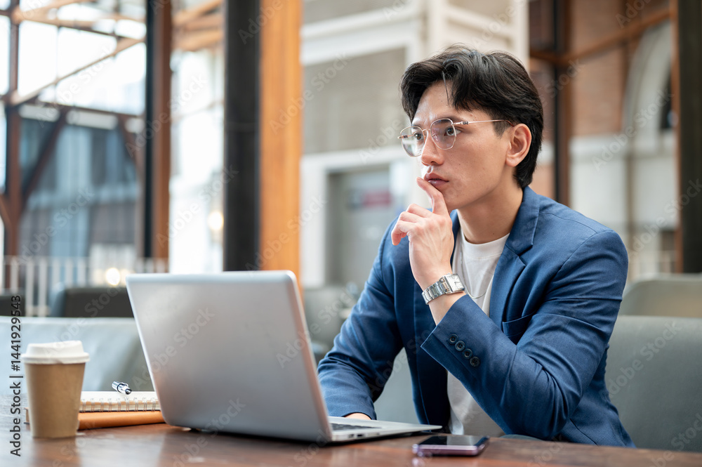 Blue suit asian man thinking thoughtfully in front of a laptop while sitting in cafe or coffee shop. Blue suit asian man thinking thoughtfully in front of a laptop while sitting in cafe or coffee shop.