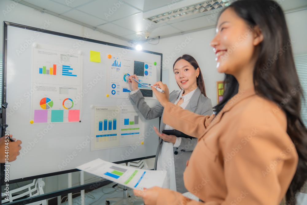 Obraz premium Two asian businesswomen analyzing graphs and charts using sticky notes on a whiteboard during a meeting in the office discussing company strategy and planning