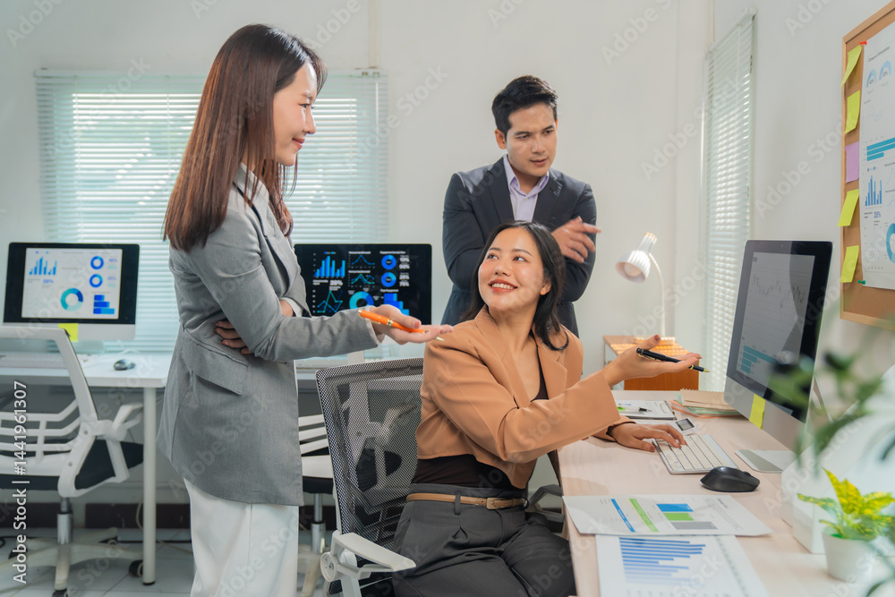 Obraz premium Three Asian businesspeople discussing in a modern office, analyzing financial charts and data on computer screens and printed documents for effective collaboration