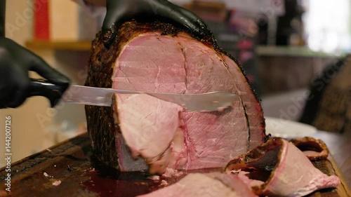  Close-up of a chef wearing black gloves slicing a large, juicy roast beef on a wooden board with a sharp knife, with visible meat texture and juices