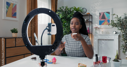 A beauty blogger films a makeup tutorial for social media. She opens a powder box, smells the product, and gently applies it to her face with a large soft brush.