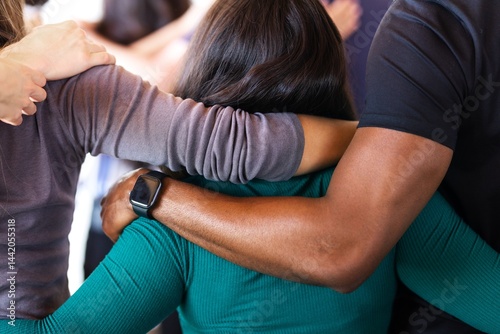 Group of diverse people with arms around hugging each other, showing unity and support. Close-up of hugging arms and shoulders, emphasizing connection and togetherness.