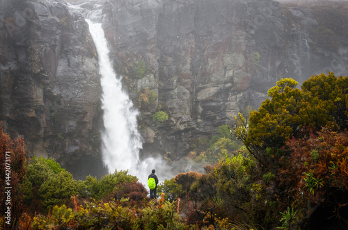 Hiker looking at the beautiful Taranaki Falls in the rain. Tongariro National Park. New Zealand.