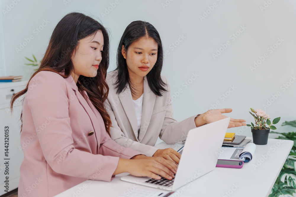 Two Asian businesswomen working together at a desk, focused and professional. They collaborate on tasks, share ideas Two Asian businesswomen working together at a desk, focused and professional. They collaborate on tasks, share ideas