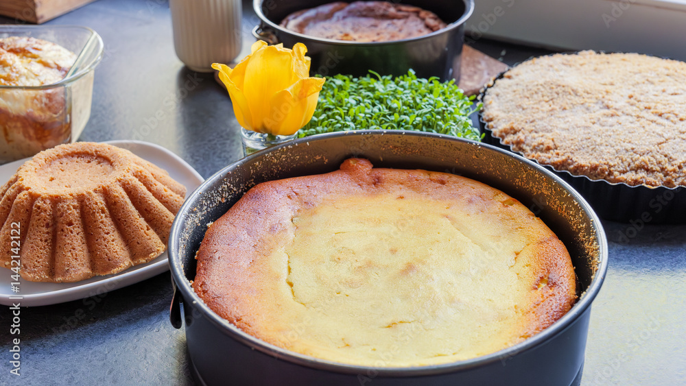 Holiday baking. Pound cake and cheesecake in a baking tin surrounded by a green plant, a yellow flower on an anthracite countertop.