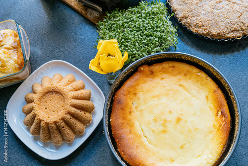 Obraz na płótnie Holiday baking. Pound cake and cheesecake in a baking tin surrounded by a green plant, a yellow flower on an anthracite countertop. w salonie