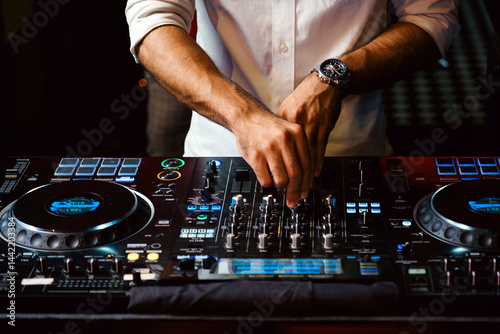 Obraz na plátně Close-up of male DJ mixing music on a professional sound console in a dimly lit club setting, highlighting nightlife energy, party vibes, and entertainment technology for modern music scenes