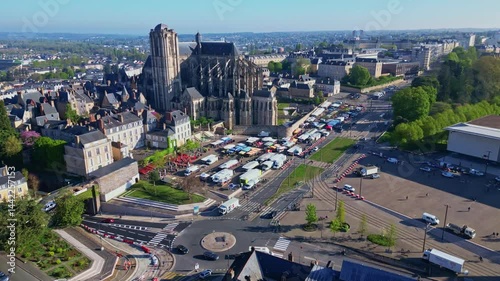 Forward drone motion over roundabout and Jacobins Market, leading to Le Mans Cathedral of Saint Julian under blue skies. France