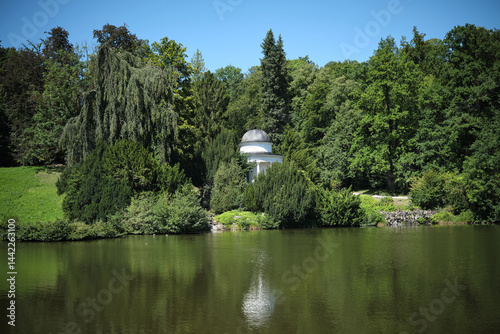Obraz na płótnie This is a tranquil and picturesque park featuring a beautiful gazebo situated by a serene lake w salonie