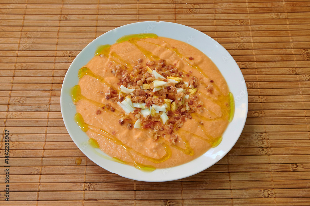 A white plate with a delicious red soup topped with bacon bits. The bacon is spread out across the surface of the soup, creating a visually appealing presentation