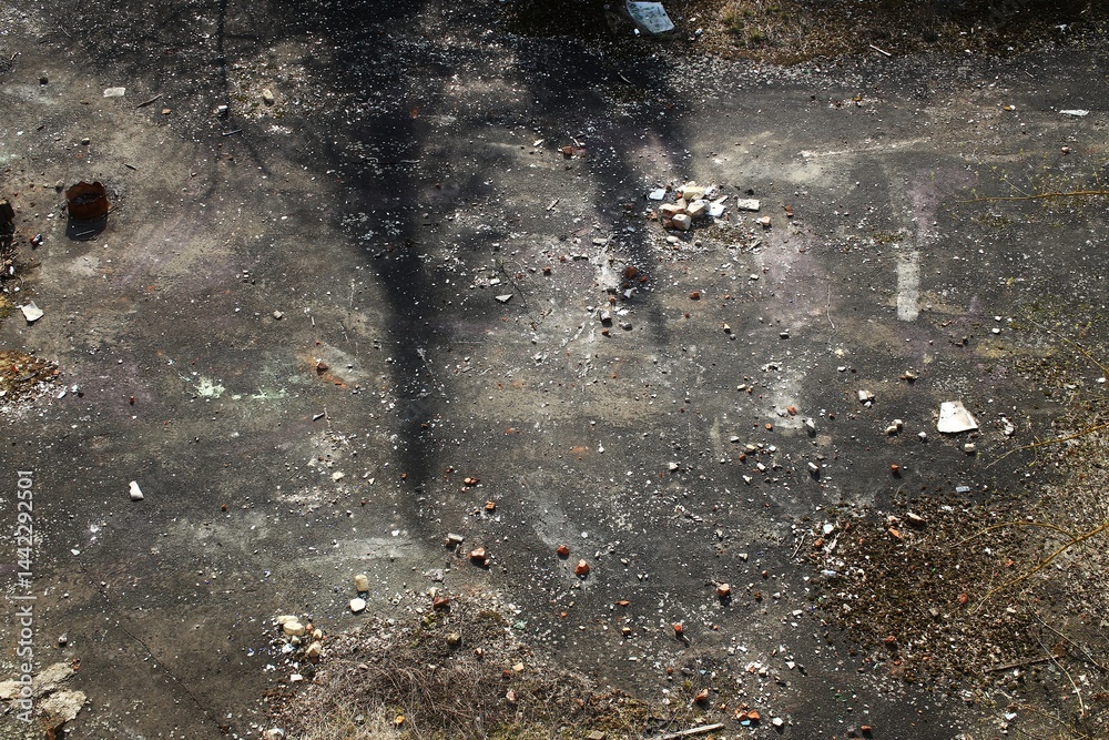 Shadowed concrete ground with scattered rubble, dry brush, and faint surface markings