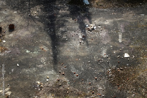 Obraz na płótnie Shadowed concrete ground with scattered rubble, dry brush, and faint surface markings w salonie