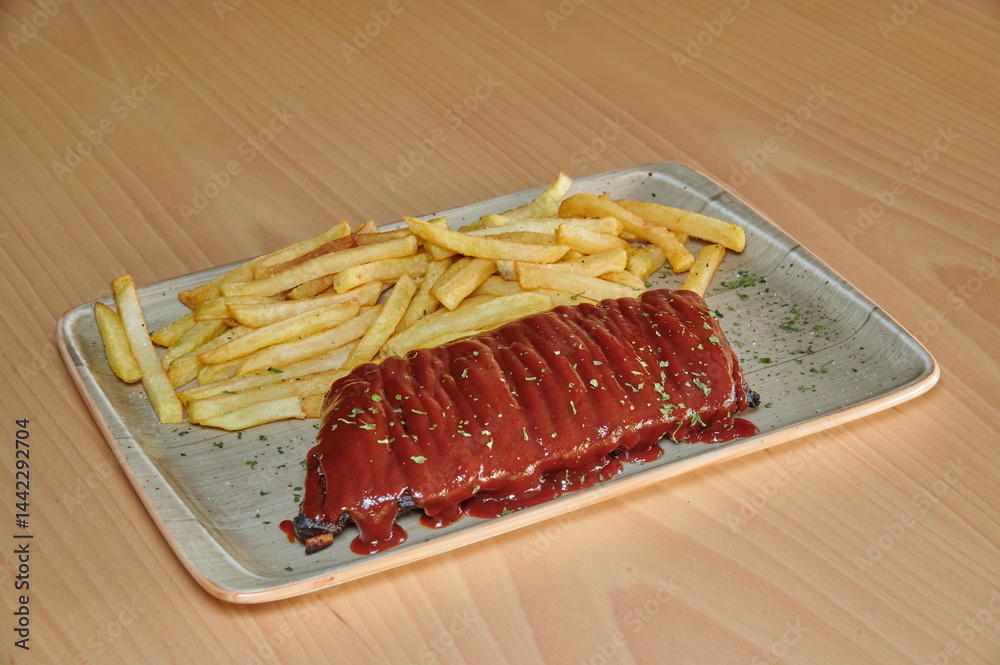A plate of ribs and french fries. The fries are cut into strips and are covered in sauce