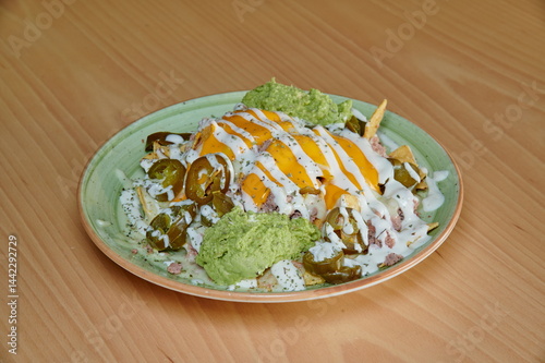 A plate of food with a green sauce on top of it. The sauce is made of avocado and cheese. The plate is on a wooden table