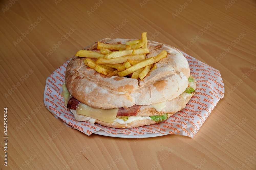 A sandwich with french fries on top of it. The sandwich is on a paper plate. The fries are cut in half