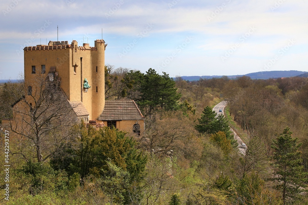 Castle Roseburg in the Harz mountains overlooking forest with winding road and distant hills under a lightly clouded sky