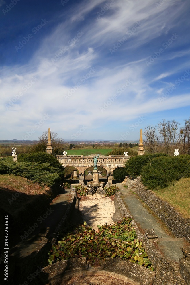 Ornate stone bridge at castle Roseburg framed by statues and green hedges with open countryside beyond