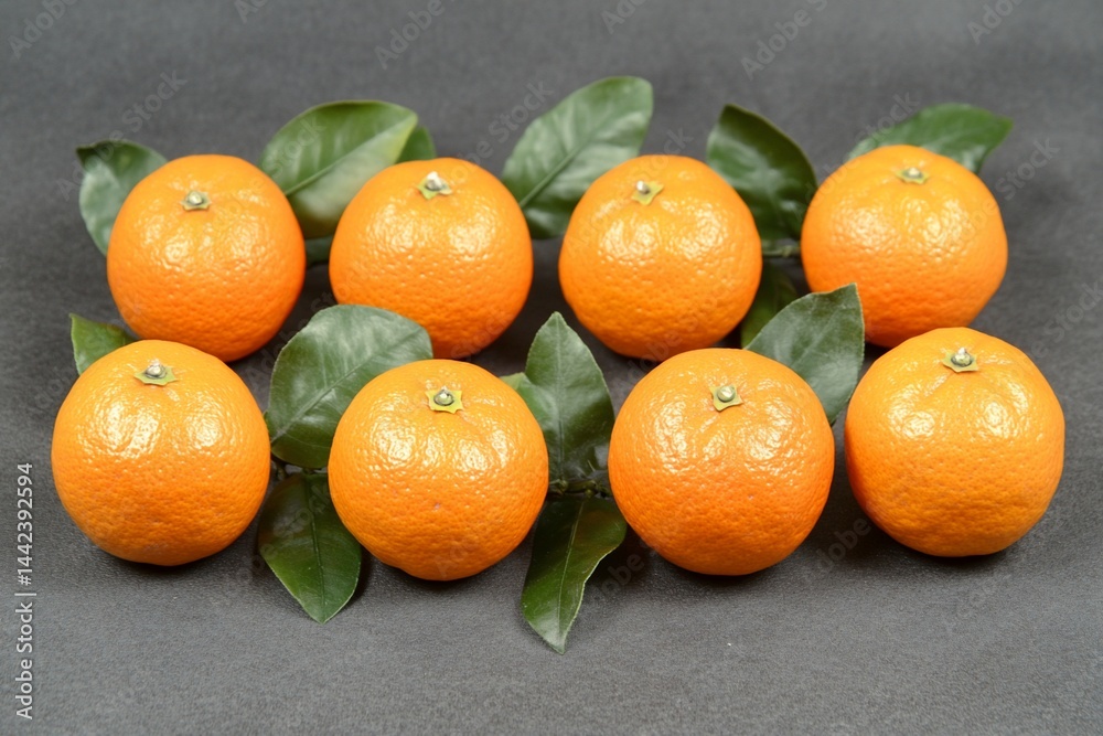 Eight ripe mandarins with green leaves arranged on a dark gray background.