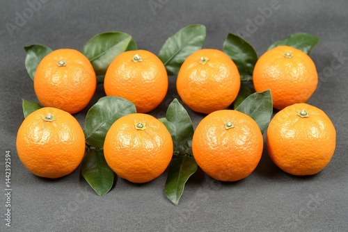 Obraz na płótnie Eight ripe mandarins with green leaves arranged on a dark gray background. w salonie