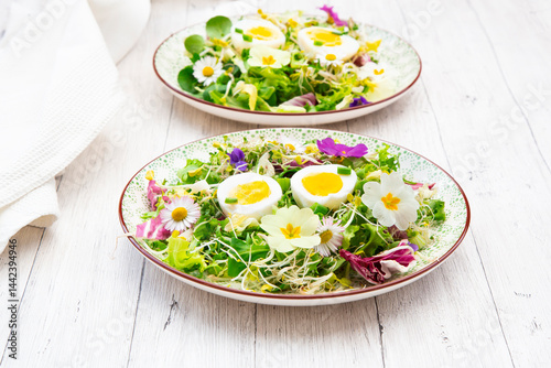 Spring salad with eatable flowers and hard boiled eggs on a wooden table