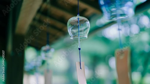 Japanese glass wind chime (Furin) hanging under eaves footage, blurred green background. Symbolizing summer traditions, tranquility and gentle sounds in Japan. Scene of peaceful garden atmosphere.