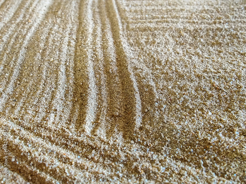 Traces in sand from rake, smooth furrows illuminated by rays of rising sun. Surface of sandy beach cleared of trash. Copy space for text.
