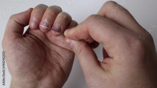 A man files the nails of his left hand with a metal file while holding it over a white table