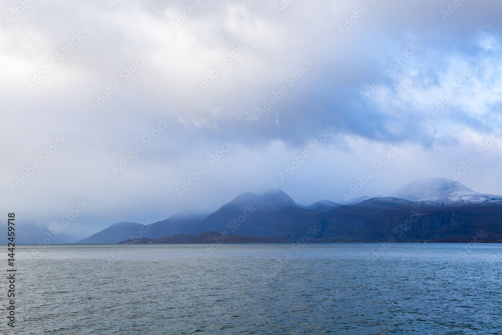 Autumn landscape of the Lyngen Alps in Northern Norway with snowy peaks, dramatic clouds, and a tranquil fjord.