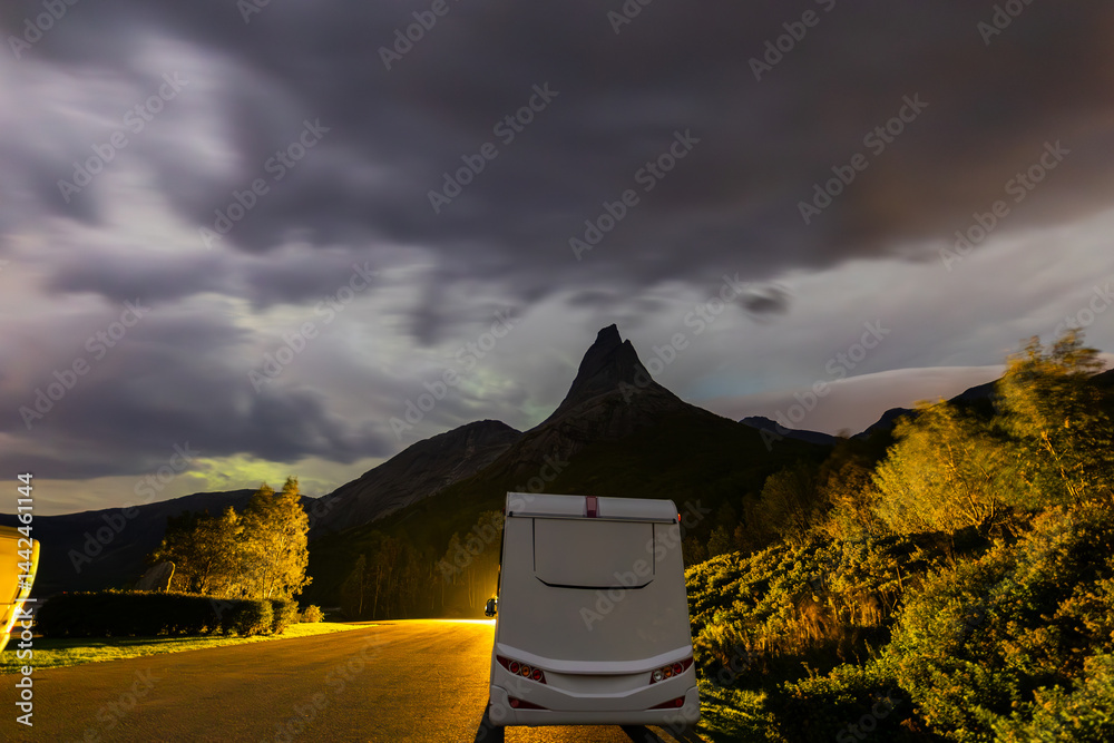 A motorhome parked under the stunning Northern Lights in Lofoten Islands, Norway, with colorful auroras in the sky.