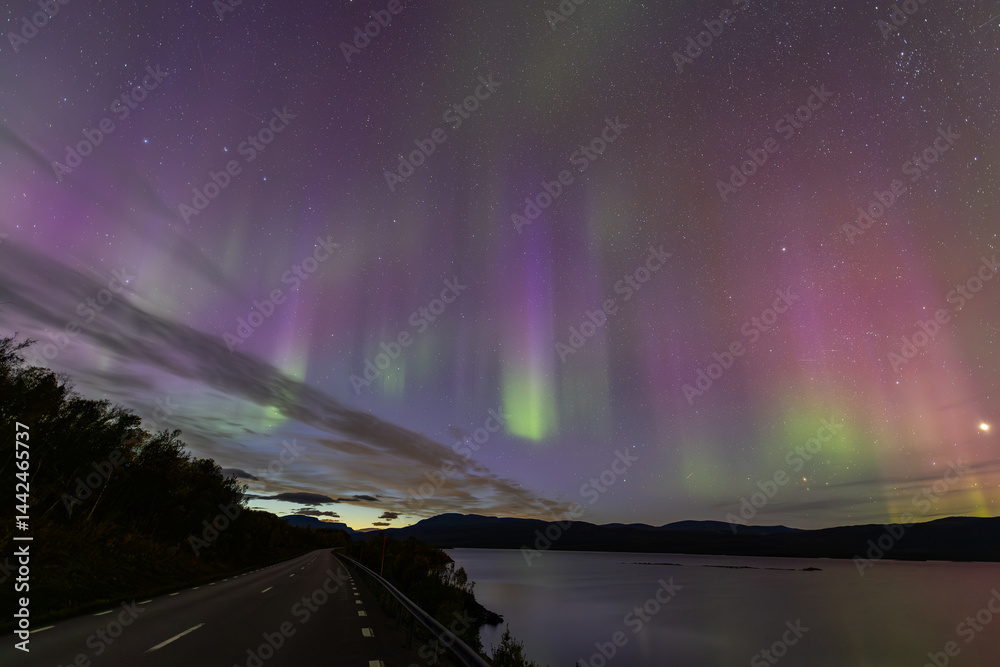 Northern lights in Kiruna, Sweden, reflecting on calm water in September with stars and forest in the background.