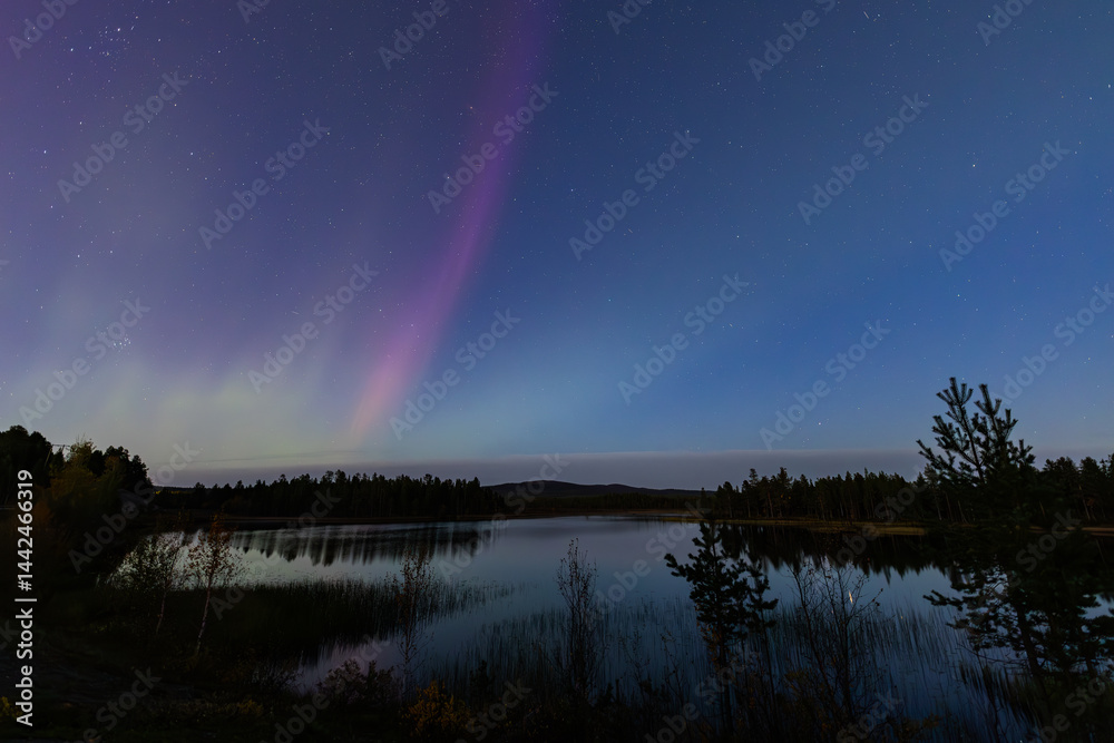 Northern lights in Kiruna, Sweden, reflecting on calm water in September with stars and forest in the background.