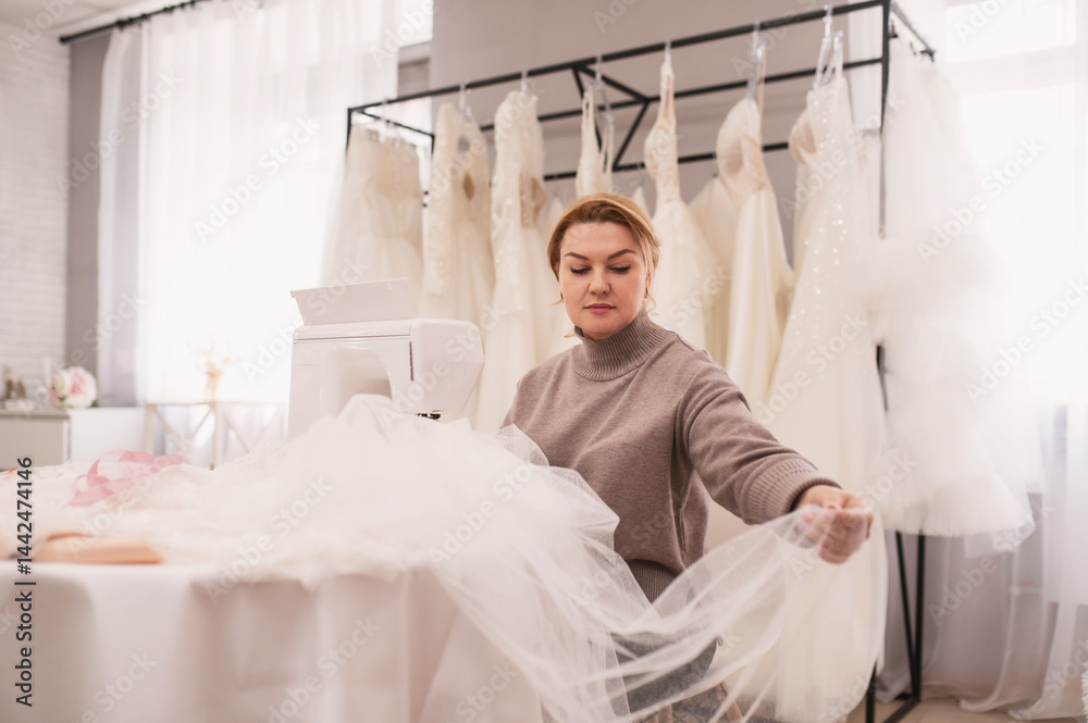 Obraz premium Portrait of seamstress in a wedding salon sews a wedding dress and veil, handmade, boutique. Small local business, self-employment.