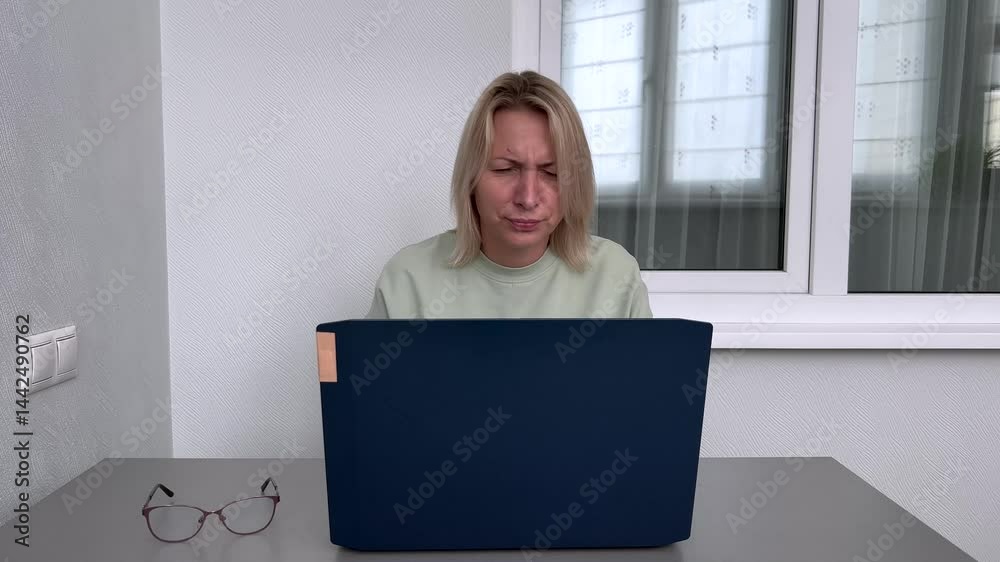 Mature woman with age-related vision struggles squints at laptop, dons corrective eyewear, resumes confident typing. Home office computer task, eyewear necessity, problem-solving focus.