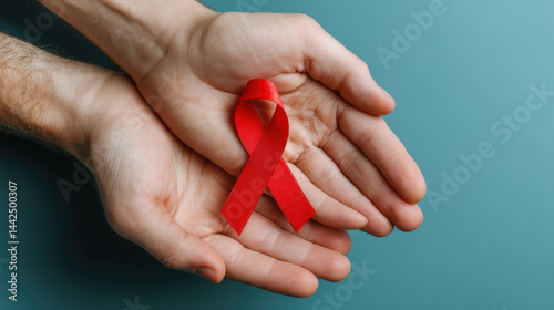 A high-quality image featuring red hiv awareness ribbon in hand over light blue background, ideal for creative, commercial, or editorial purposes.