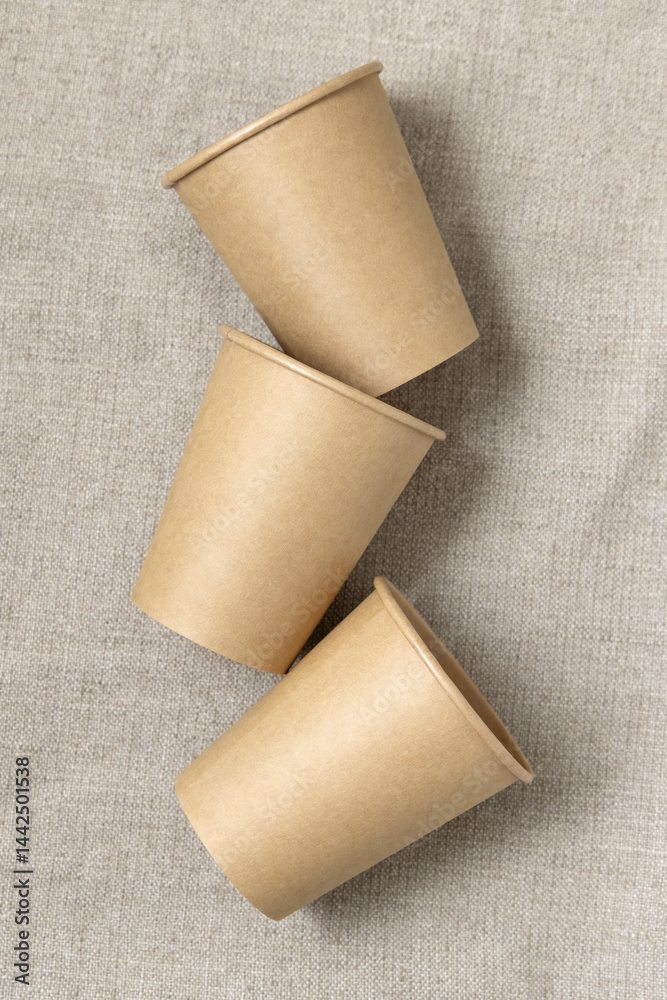 Disposable beige paper cups on a beige linen cloth top view, mockup. No plastic lifestyle