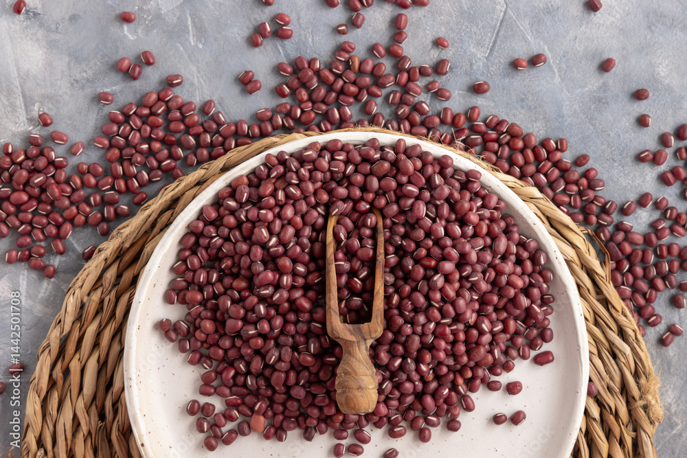Plate full of dried red azuki beans with a wooden scoop top view. East Asian legumes, vegetarian food