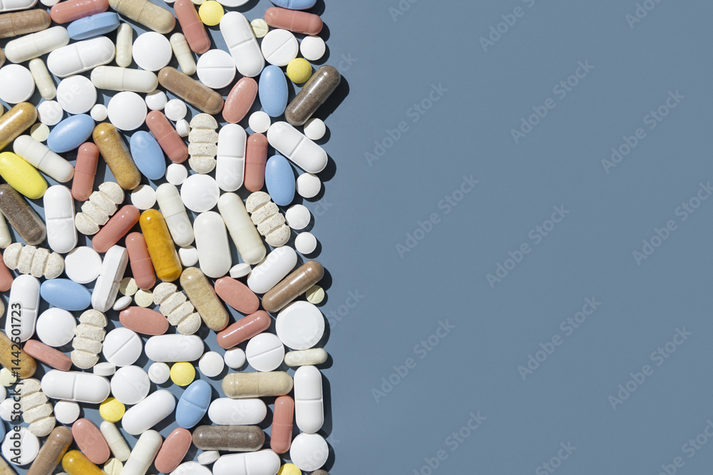 Pile of mixed white, yellow and blue medical capsules and pills on blue top view, border