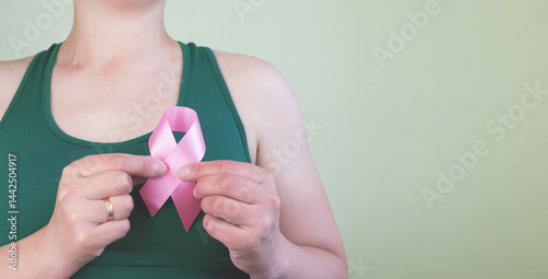 Young woman holding pink ribbon on green background with space for text.