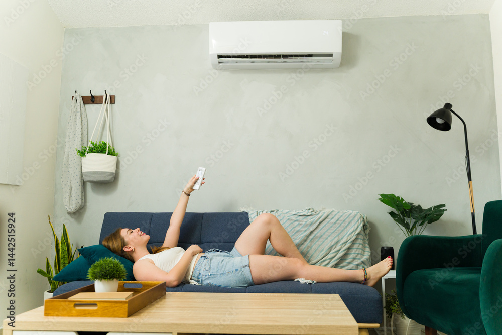 Woman relaxing on sofa using remote control for air conditioner