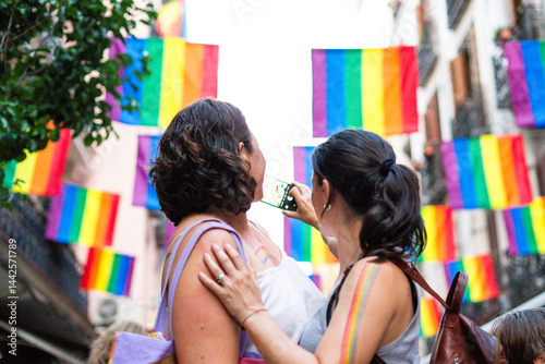Women taking pictures during gay pride parade with rainbow flags photo