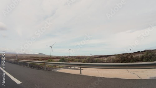 View of wind turbines installed across the field in Spain from a moving car during a cloudy day, handheld shot. Wind farms and energy concepts.